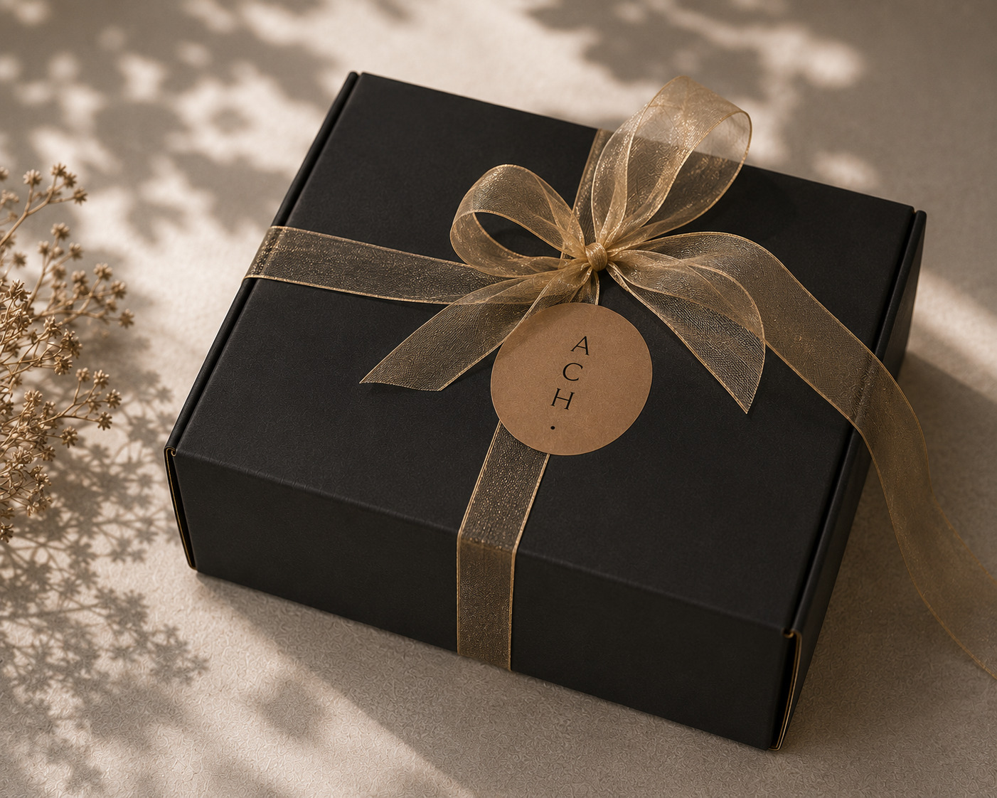 ACH packaging: black gift box tied with a sheer gold ribbon and kraft seal, styled with dried botanicals